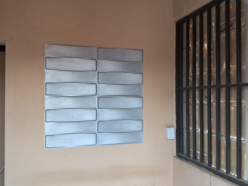 A utilitarian interior space featuring a wall-mounted metal panel, security bars over the window, and a single light switch.