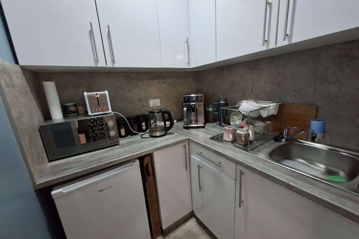 Compact kitchenette featuring white cabinetry, grey stone-look countertops, a stainless steel sink, and integrated space for a small under-counter refrigerator.