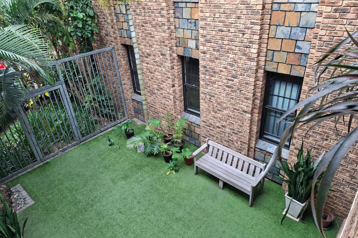 A private courtyard area featuring artificial turf, brick facade walls, and secure metal perimeter fencing.