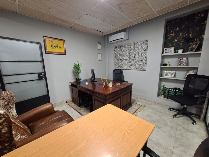 A professional office space featuring tiled flooring, a suspended ceiling, built-in wall shelving, and a wall-mounted air conditioning unit.