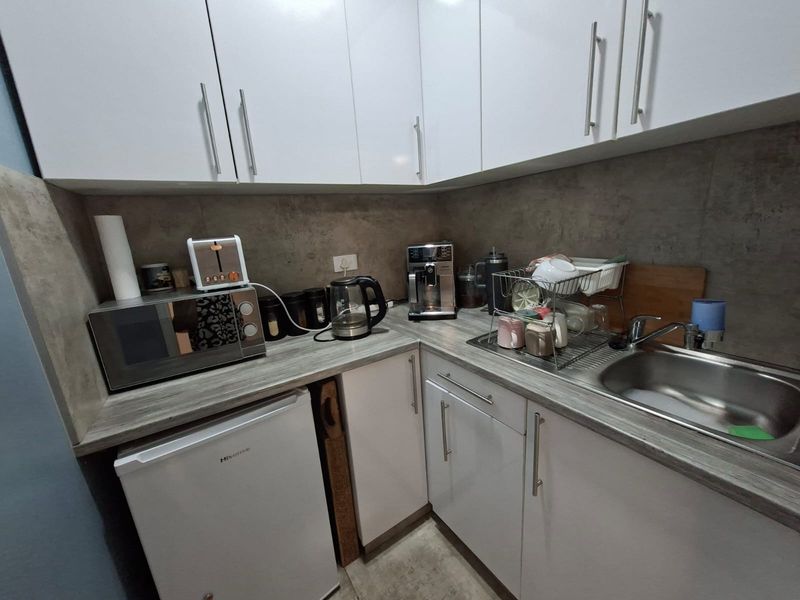 Compact kitchenette featuring white cabinetry, grey stone-look countertops, a stainless steel sink, and integrated space for a small under-counter refrigerator.