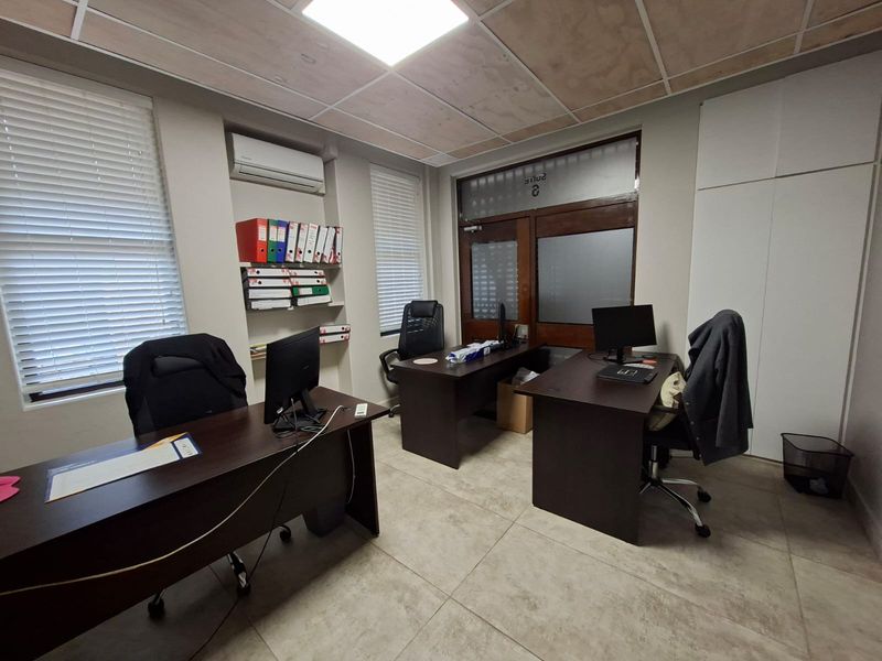A functional office space featuring tiled flooring, built-in shelving, integrated air conditioning unit, and a wooden framed glass entrance door.