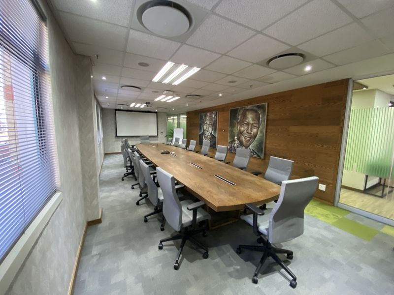 A professional boardroom featuring a large wooden conference table, suspended ceiling with recessed lighting, wood-paneled feature wall, and integrated projector screen.