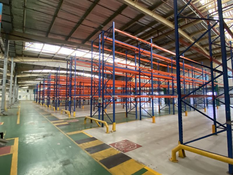Spacious industrial warehouse featuring high-clearance ceilings, extensive steel racking systems, durable epoxy flooring, and natural light provided by integrated skylights.