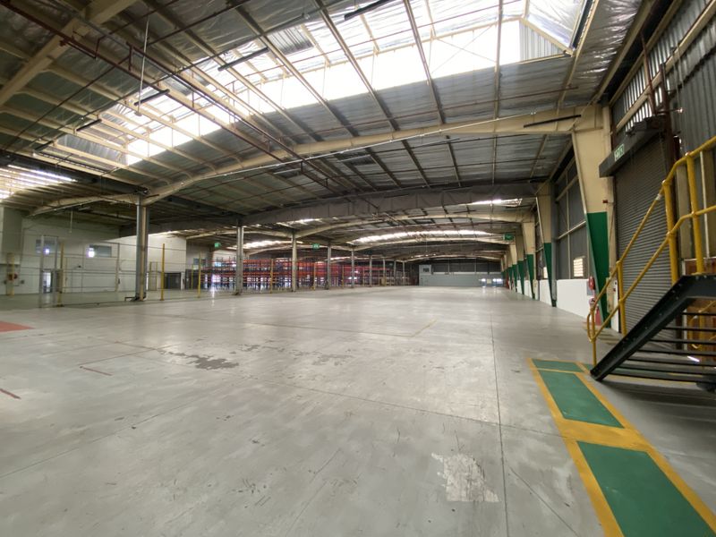 Spacious industrial warehouse featuring high ceilings with integrated skylights, concrete flooring, and a metal staircase, providing a versatile open-plan storage or manufacturing environment.