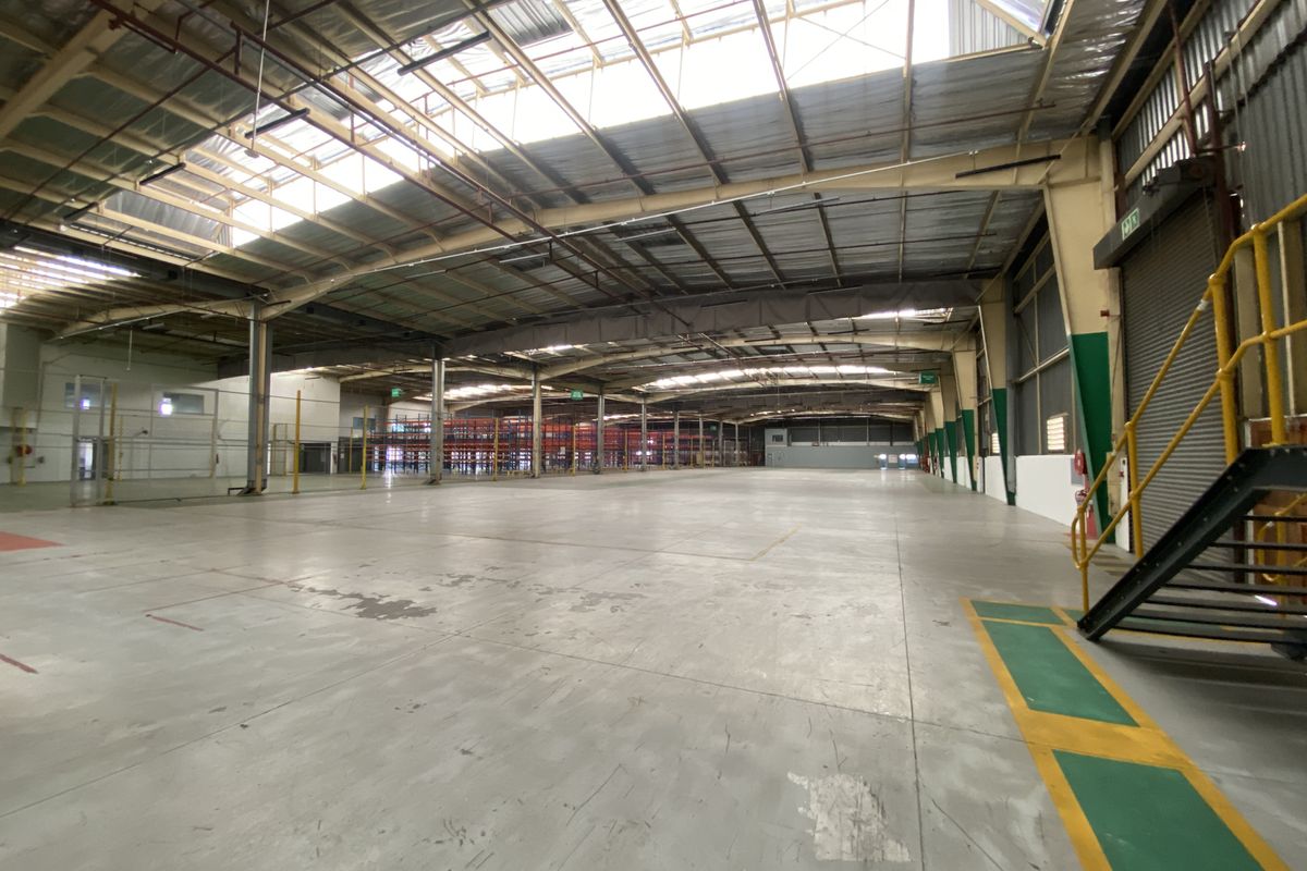 Spacious industrial warehouse featuring high ceilings with integrated skylights, concrete flooring, and a metal staircase, providing a versatile open-plan storage or manufacturing environment.