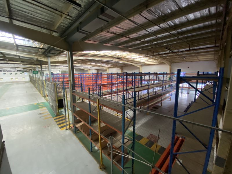 Large industrial warehouse space featuring high ceilings with skylights, durable epoxy flooring, and extensive built-in steel racking systems for storage.