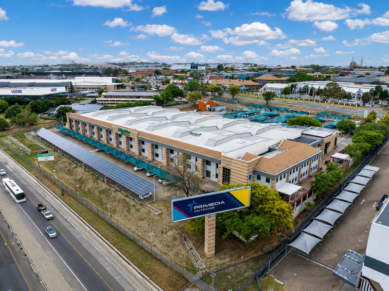 Aerial view of a large industrial facility featuring extensive solar panel installations, shaded parking areas, and prominent roadside signage.