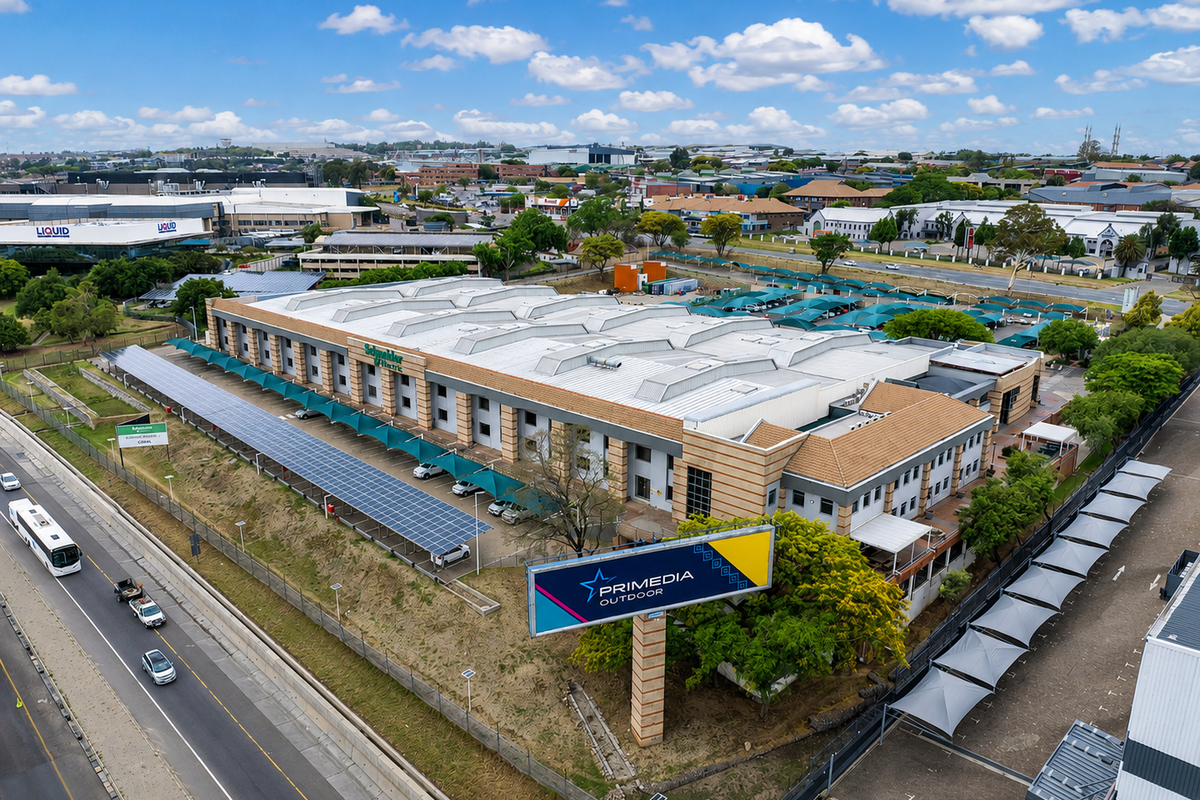 Aerial view of a large industrial facility featuring extensive solar panel installations, shaded parking areas, and prominent roadside signage.