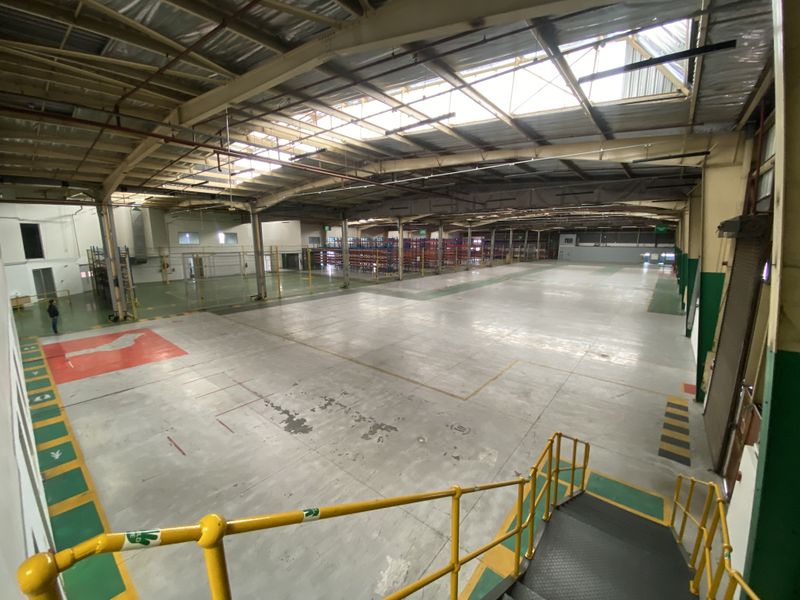 Expansive industrial warehouse space featuring high ceilings with integrated skylights, concrete flooring, and a mezzanine access staircase with safety railings.