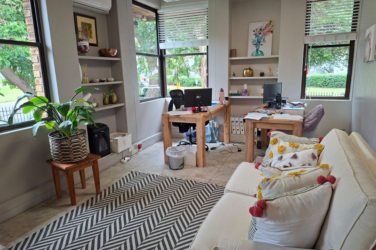 A bright office space featuring built-in shelving, tiled flooring, large windows with blinds, and a wall-mounted air conditioning unit.