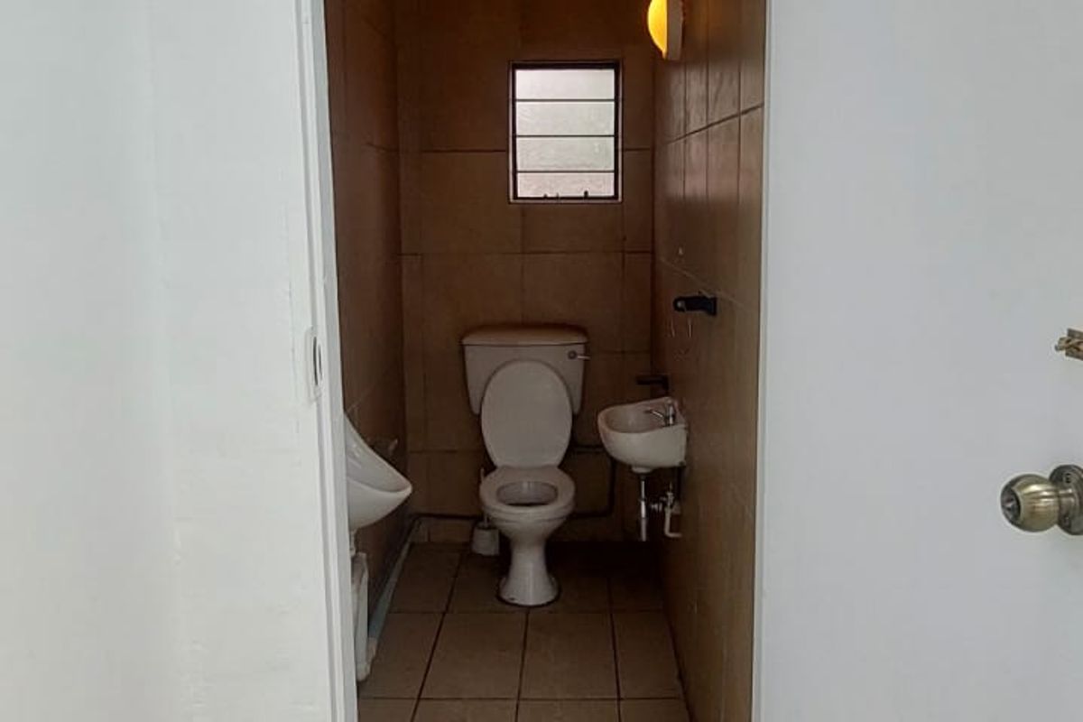 A compact restroom facility featuring a toilet, wall-mounted basin, and urinal with tiled walls and flooring.