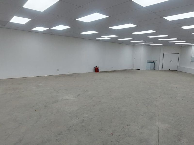 A spacious, open-plan retail unit featuring a suspended ceiling with recessed lighting, white walls, and an unfinished concrete floor.