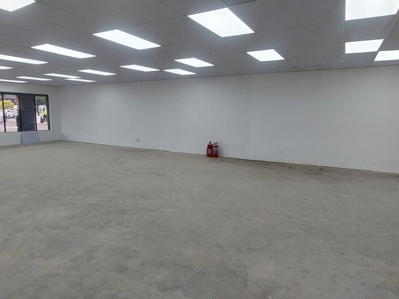 A spacious, open-plan retail unit featuring a suspended grid ceiling with recessed lighting, large display windows, and an unfinished concrete floor.