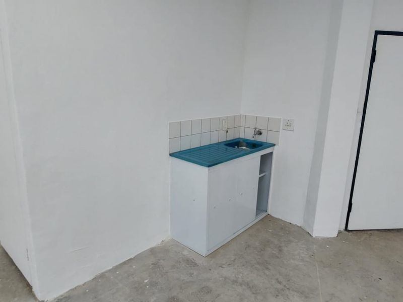 A basic utility area featuring a small sink unit with tiled splashback, set against plain white walls and concrete flooring.
