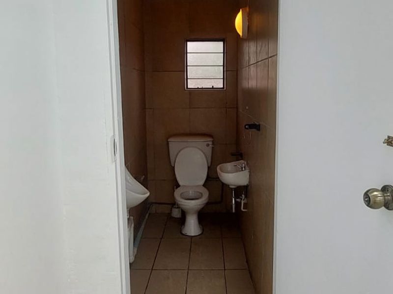 A compact restroom facility featuring a toilet, wall-mounted basin, and urinal with tiled walls and flooring.