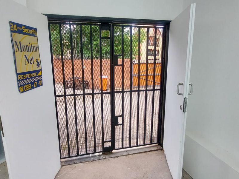 A functional utility space featuring a built-in sink, cabinetry, and a secure metal security gate leading to an outdoor area.