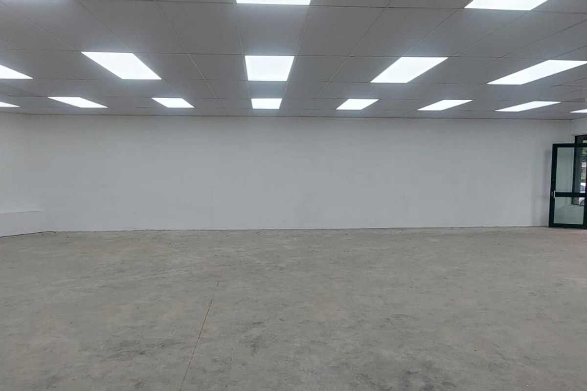A spacious, open-plan retail unit featuring a concrete floor, recessed drop ceiling with integrated lighting, and a glass entrance door.