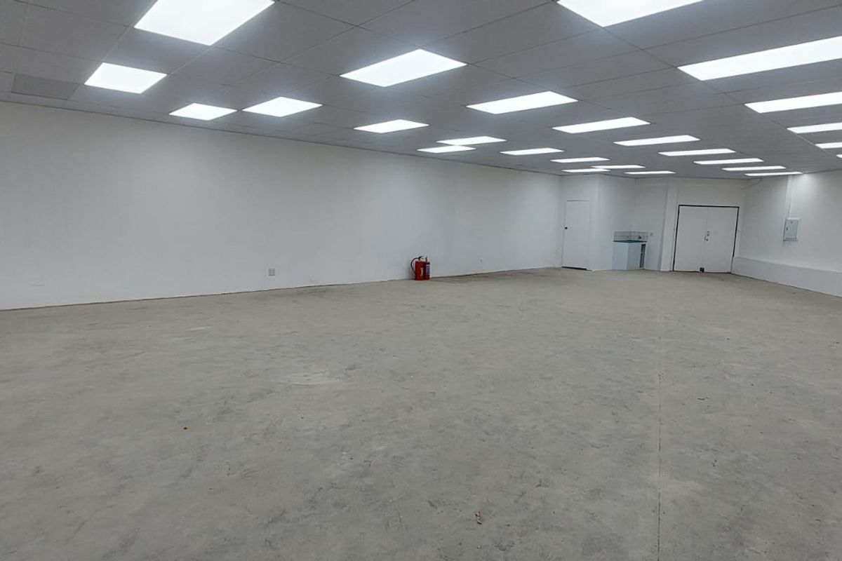 A spacious, open-plan retail unit featuring a suspended ceiling with recessed lighting, white walls, and an unfinished concrete floor.