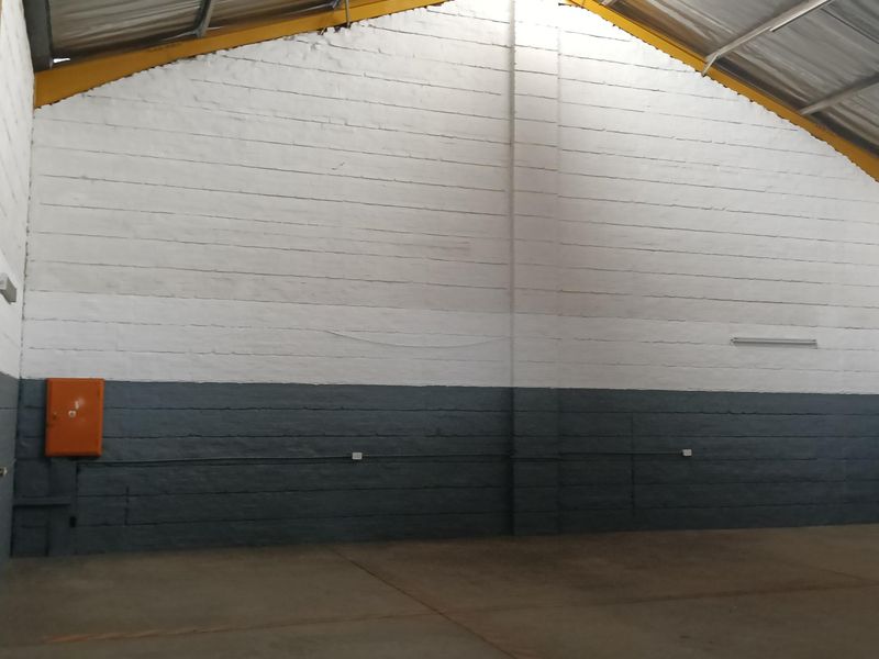 Spacious industrial warehouse interior featuring high ceilings, exposed steel roof structure, painted masonry walls, and durable concrete flooring with integrated electrical distribution box.