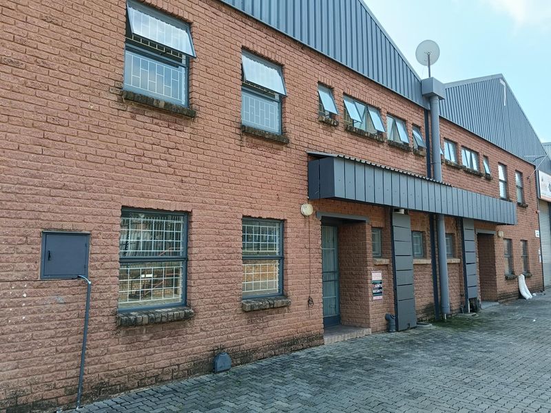 Exterior view of a two-story industrial building featuring face-brick facade, metal roof cladding, security-barred windows, and paved driveway access.