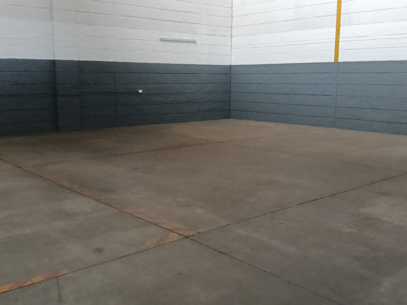 A spacious, empty industrial warehouse unit featuring high ceilings, painted concrete block walls, and durable concrete flooring, suitable for storage or light manufacturing.