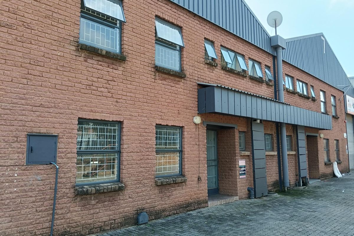 Exterior view of a two-story industrial building featuring face-brick facade, metal roof cladding, security-barred windows, and paved driveway access.