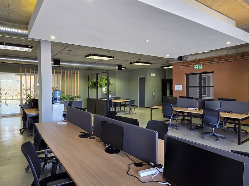 Modern open-plan office space featuring industrial-style exposed concrete ceilings, polished concrete floors, and exposed brick accents with integrated lighting and ducting.