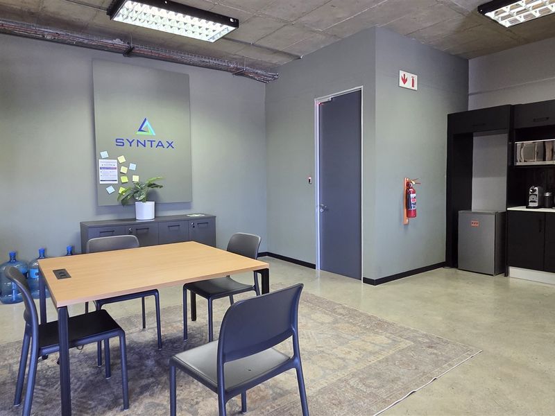 Modern open-plan office space featuring an exposed concrete ceiling, polished concrete floors, and a compact kitchenette area with built-in cabinetry.