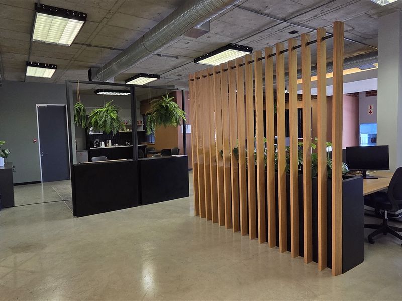 Modern open-plan office space featuring polished concrete floors, exposed industrial ceilings with ducting, and a stylish timber slat room divider.