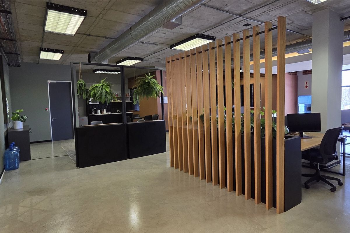Modern open-plan office space featuring polished concrete floors, exposed industrial ceilings with ducting, and a stylish timber slat room divider.