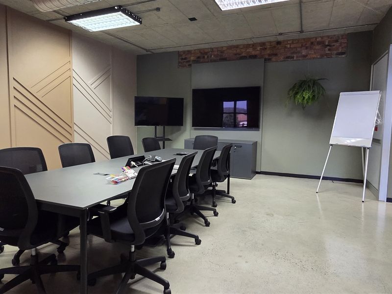 A modern, well-maintained office meeting room featuring polished concrete floors, decorative wall paneling, exposed brick accents, and integrated ceiling lighting.