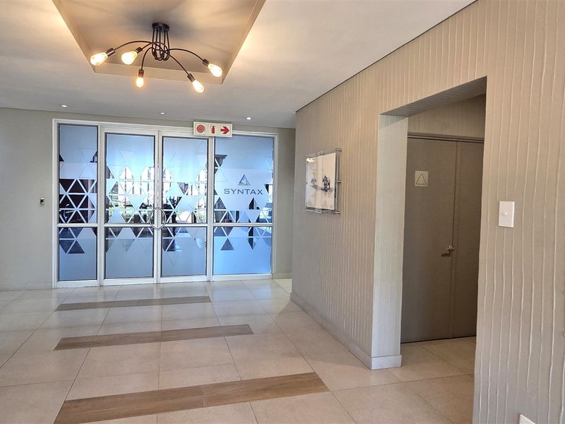 Modern office entrance lobby featuring tiled flooring, textured wall accents, recessed ceiling lighting, and glass-paneled double doors.