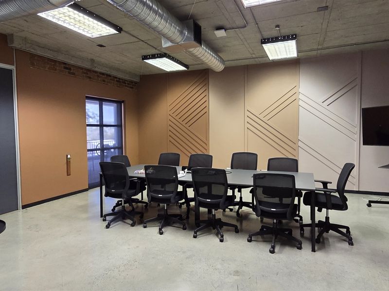 Modern office boardroom featuring an industrial aesthetic with exposed concrete ceilings, ducting, polished concrete floors, and decorative wall paneling.