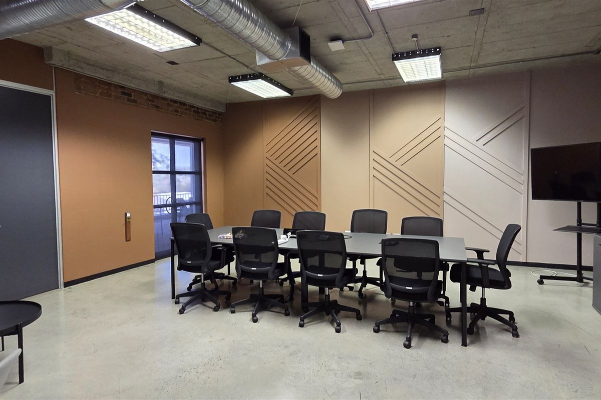 Modern office boardroom featuring an industrial aesthetic with exposed concrete ceilings, ducting, polished concrete floors, and decorative wall paneling.