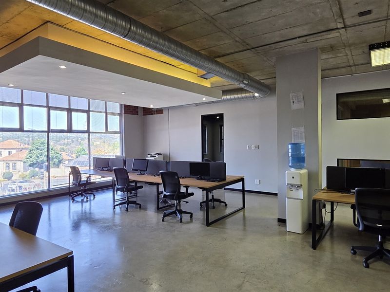 Modern open-plan office space featuring polished concrete floors, exposed industrial ceiling with ducting, and large windows providing ample natural light.
