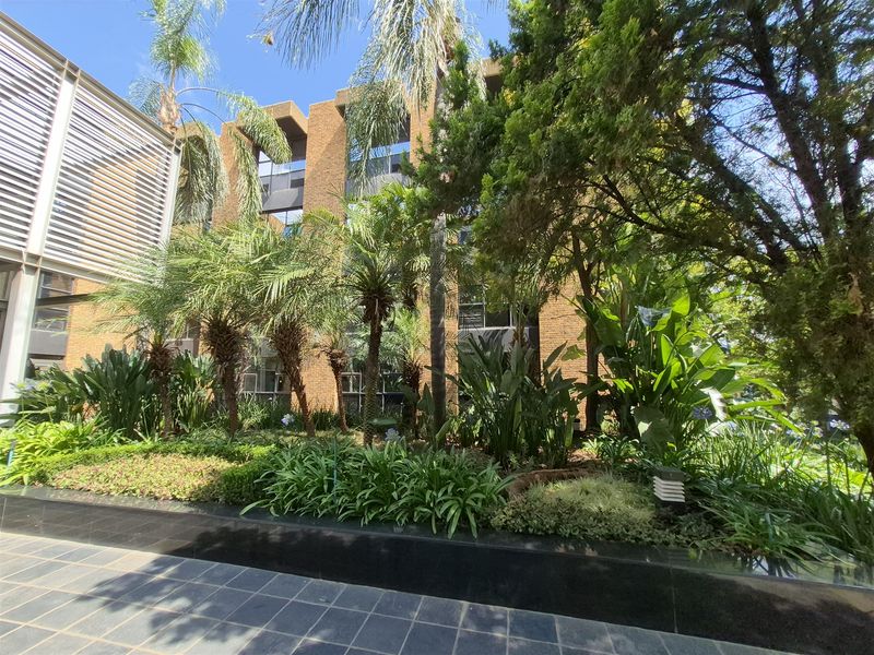 A view of the office building exterior featuring a brick facade, large windows, and a well-maintained landscaped garden area with stone paving.