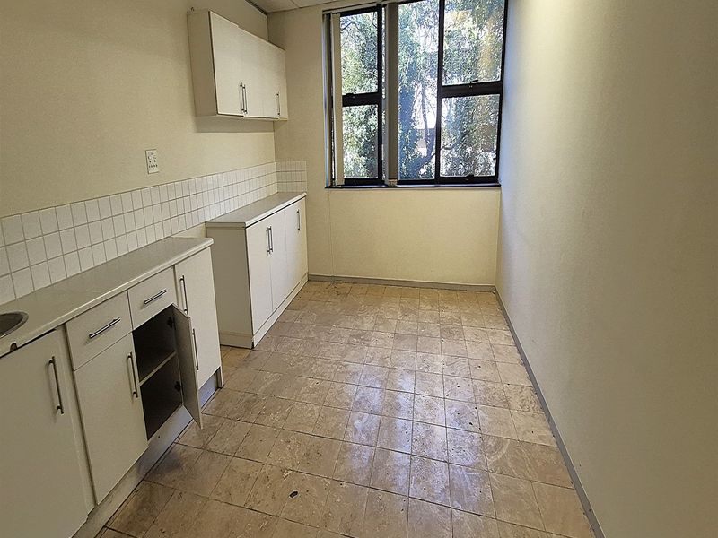 A small, empty office kitchenette featuring built-in white cabinetry, a tiled backsplash, and a large window providing natural light.
