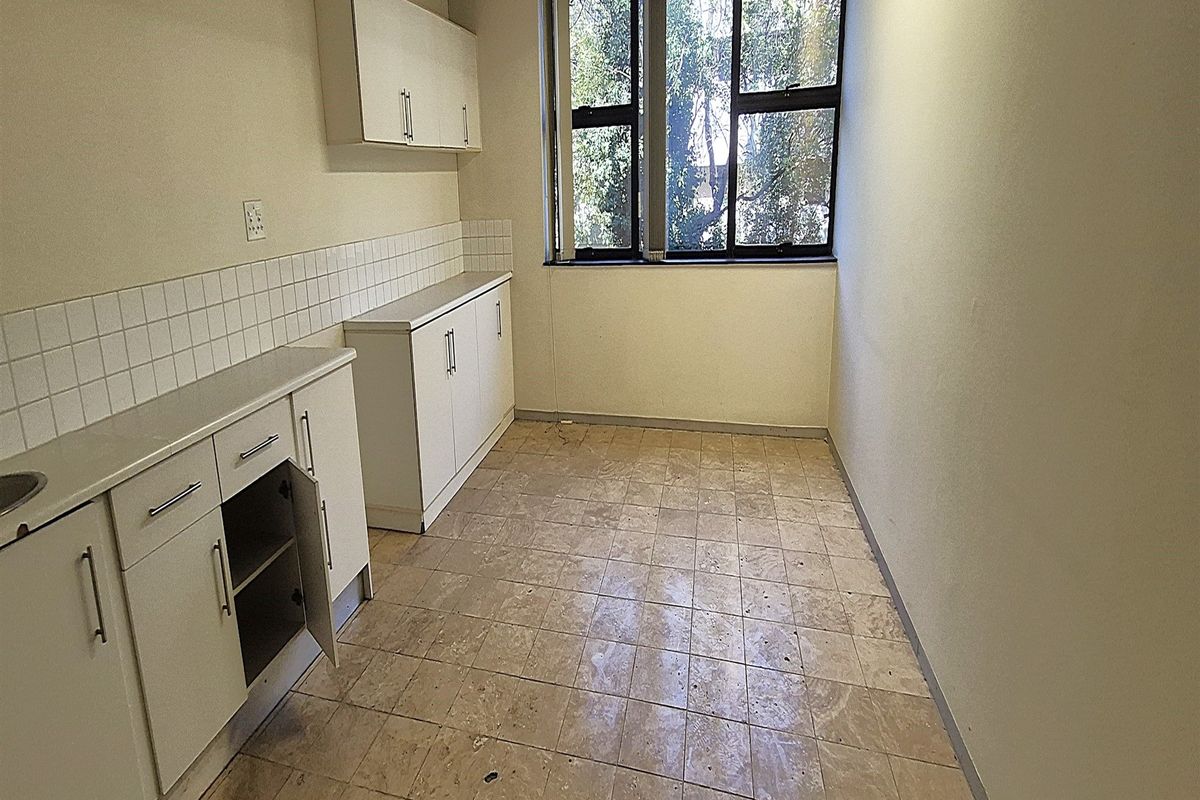 A small, empty office kitchenette featuring built-in white cabinetry, a tiled backsplash, and a large window providing natural light.