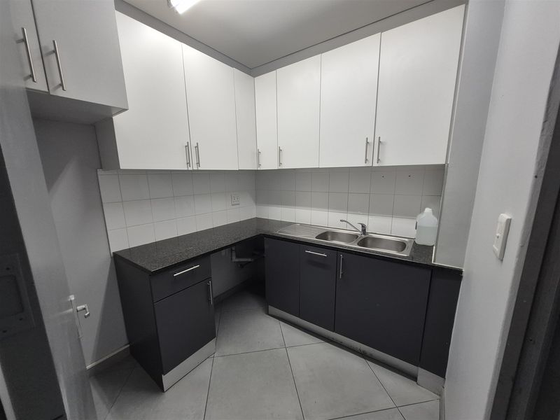 A clean and functional office kitchenette featuring modern two-tone cabinetry, granite countertops, and a double basin sink with tiled backsplash.