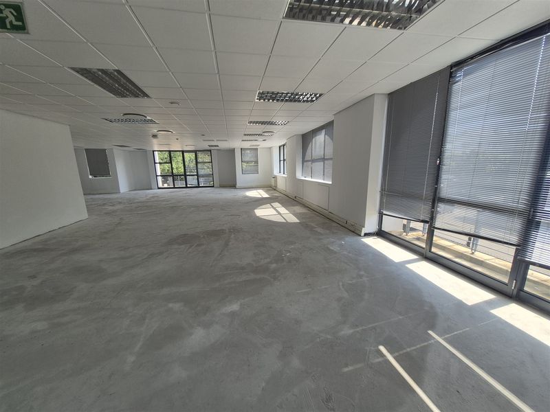 Spacious open-plan office area featuring large windows with blinds, suspended ceilings with recessed lighting, and an unfinished concrete floor ready for custom flooring installation.