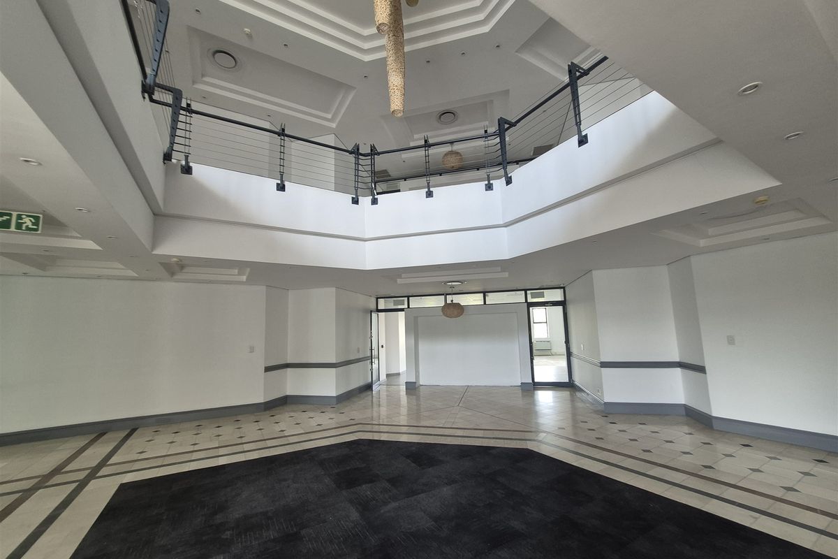 Spacious double-volume entrance foyer featuring a mezzanine level, recessed ceiling details, and elegant tiled flooring in a professional office building.