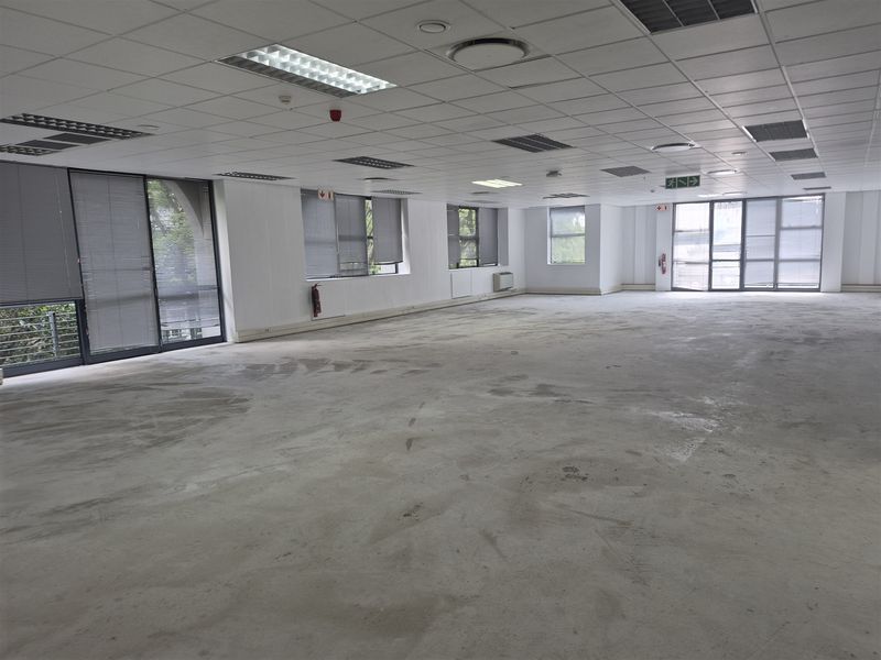 A large, open-plan office space featuring a suspended ceiling, recessed lighting, and expansive windows with blinds, currently awaiting flooring finishes.