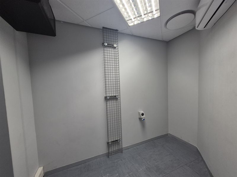 A clean, empty office space featuring vinyl flooring, a suspended ceiling with recessed lighting, an air conditioning unit, and wall-mounted cable management infrastructure.