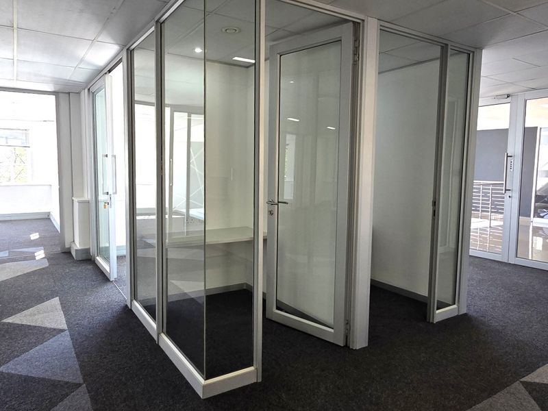 Modern office space featuring glass partition walls, aluminum framing, suspended ceilings, and patterned carpeting, providing a professional and open work environment.