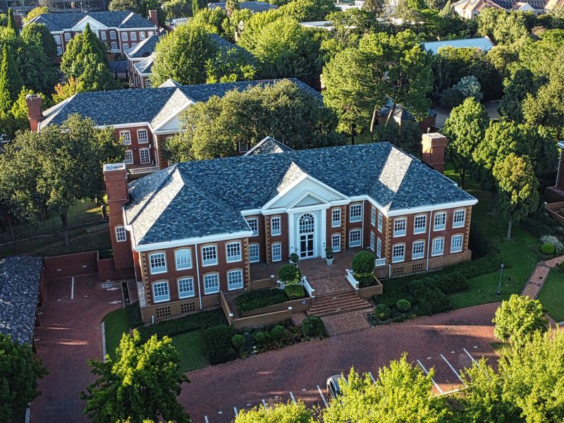 Aerial view of a professional office complex featuring classic brick architecture, slate roofing, extensive landscaped grounds, and ample paved parking facilities.