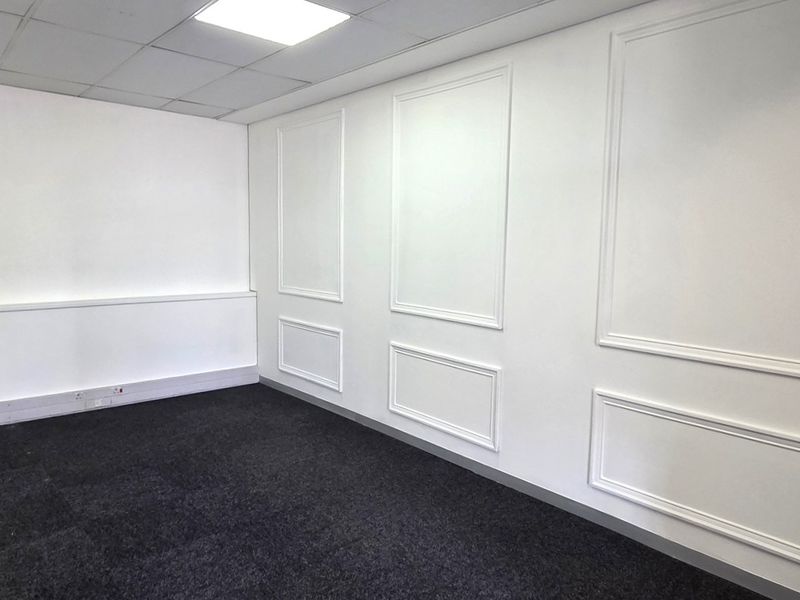 A clean, empty office space featuring decorative wall molding, dark carpet flooring, and a drop ceiling with recessed lighting.