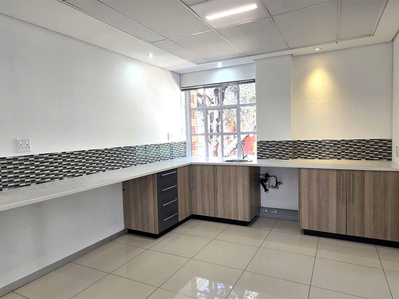 A clean, modern office kitchenette featuring laminate cabinetry, a mosaic tile backsplash, stainless steel sink, and bright recessed lighting.