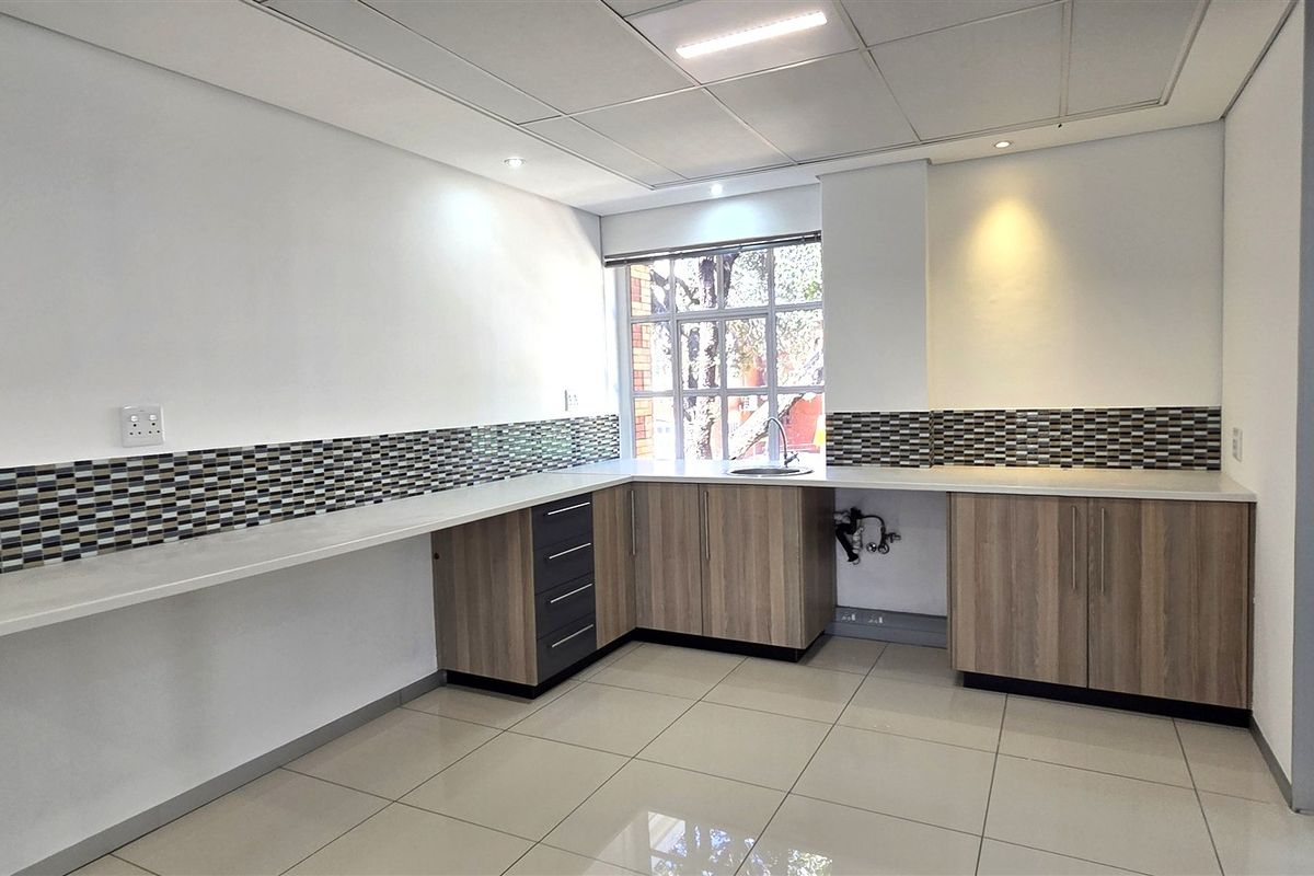 A clean, modern office kitchenette featuring laminate cabinetry, a mosaic tile backsplash, stainless steel sink, and bright recessed lighting.