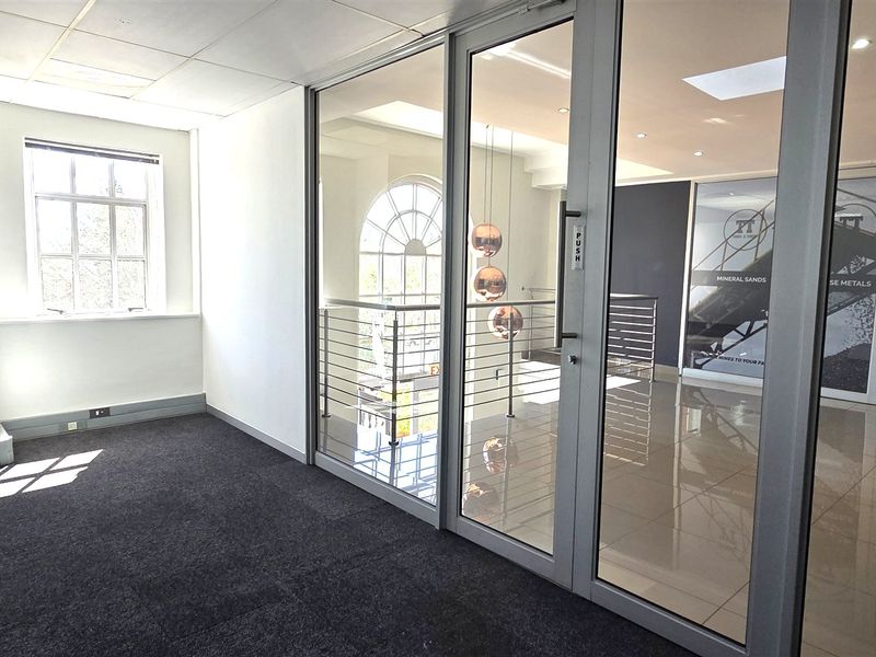 A bright, modern office space featuring glass partitions, tiled and carpeted flooring, and recessed lighting, offering a professional and clean work environment.